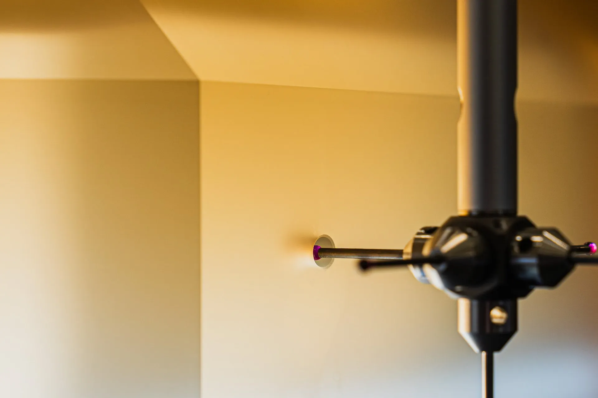 Probe with a red ruby tip measuring a hole in a part, in warm light