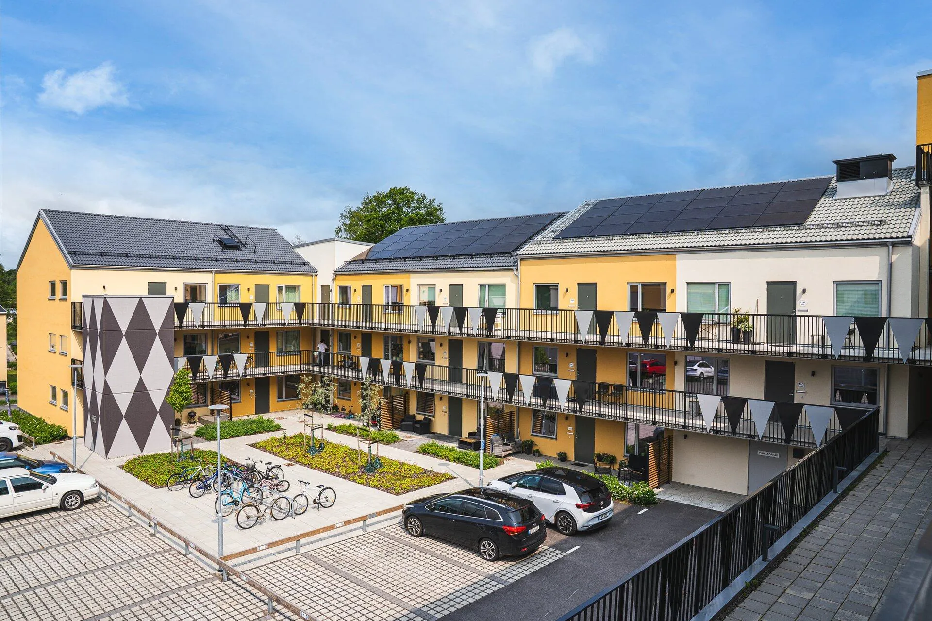 Gula flerbostadshus med solpaneler runt en innergård med cykelställ