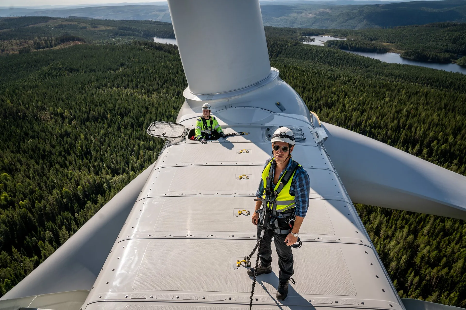 Två tekniker står på nacellen högt över Sundsvalls skogar