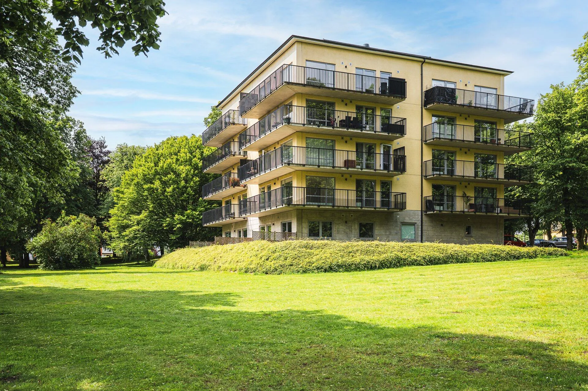 Gult flerbostadshus med balkonger i parkmiljö