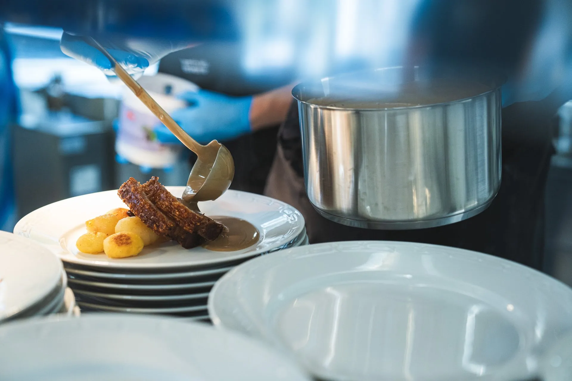 Kock öser sås över fläsk och potatis vid lunchserveringen