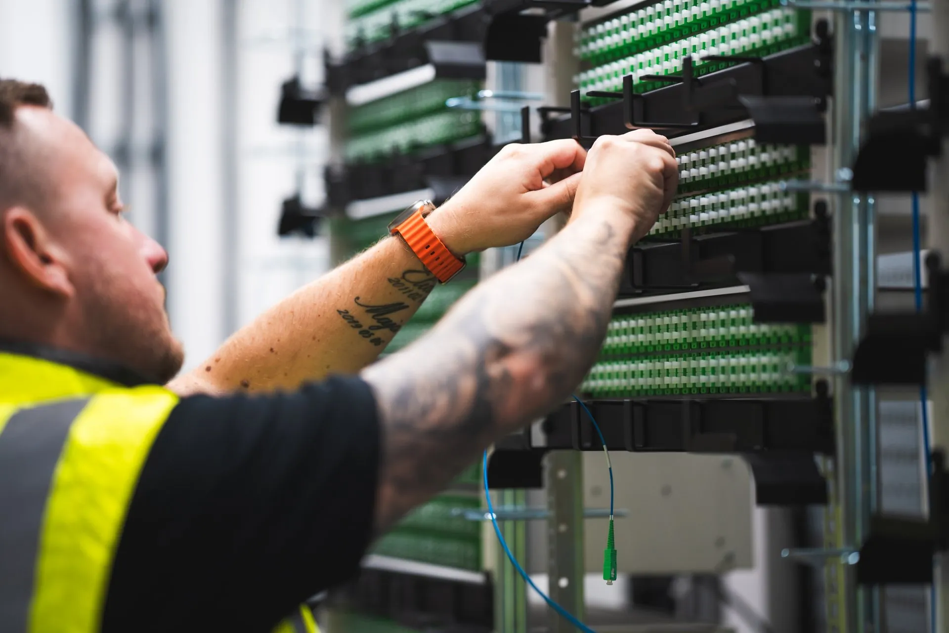 Staffanstorps Fibernät employee in a hi-vis vest working on fibre connections in a rack