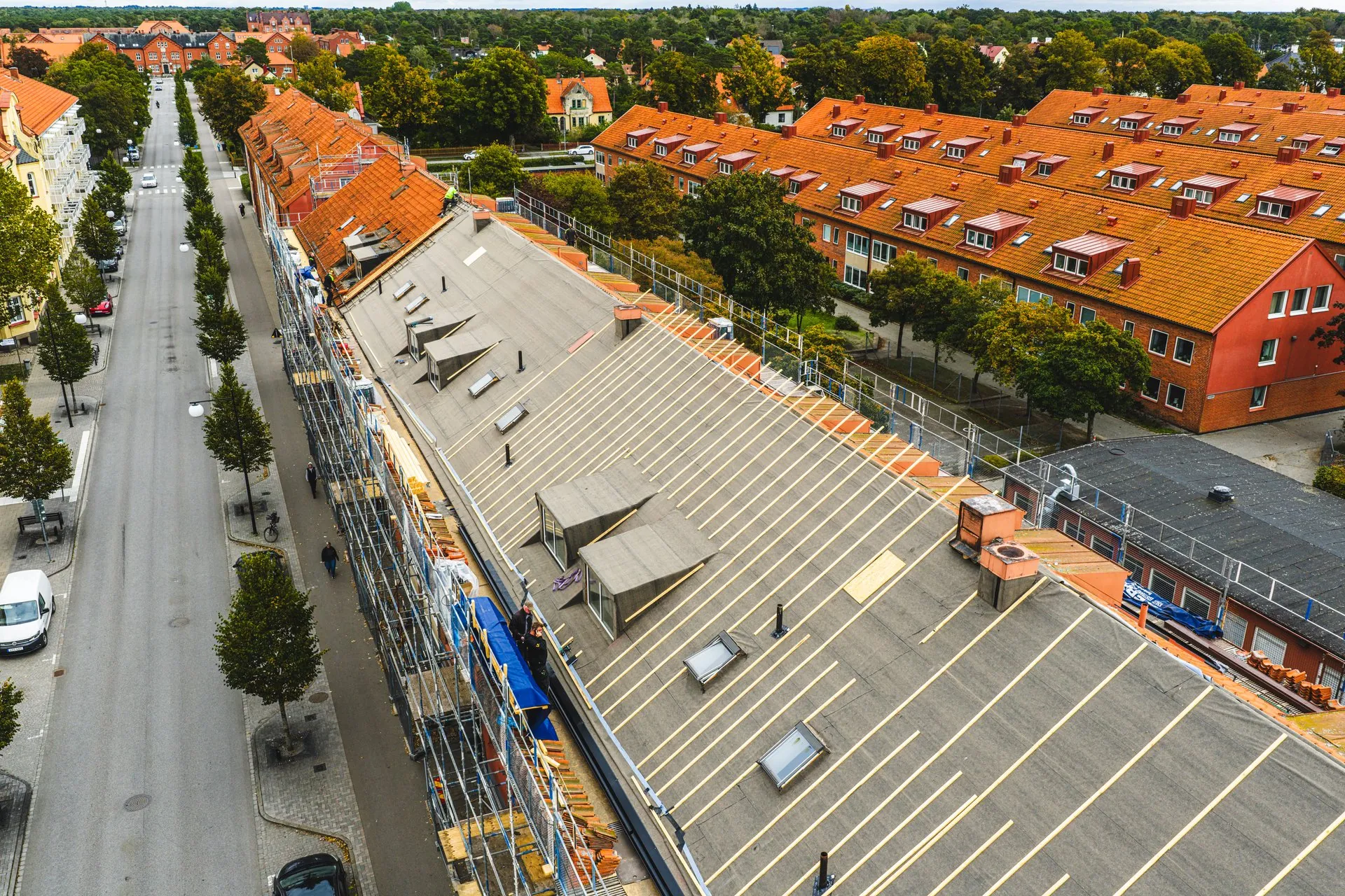 Flygfoto över takomläggning på flerbostadshus med byggnadsställningar längs gatan