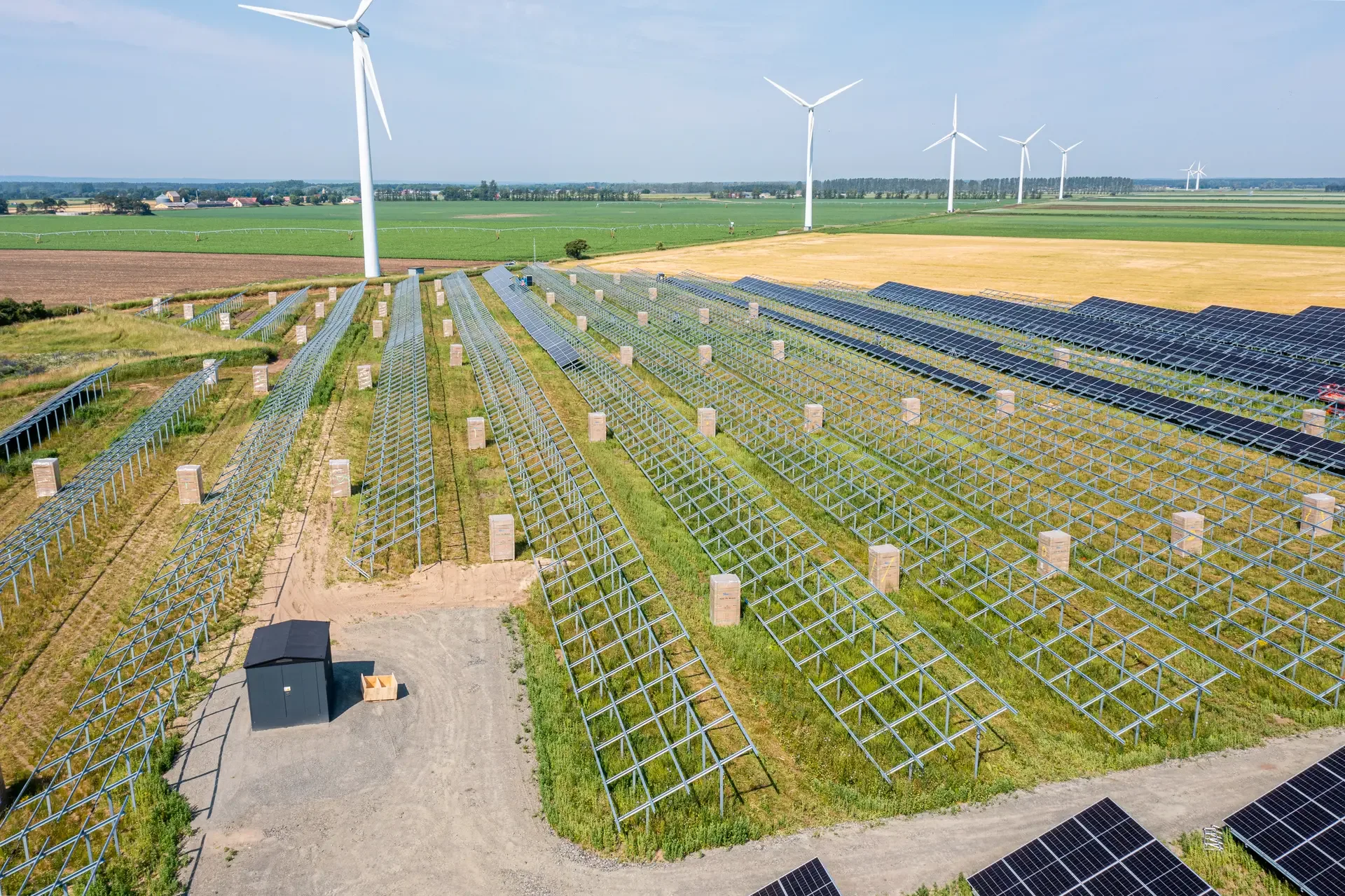 Solparken i Åhus under uppbyggnad med monteringsställningar och vindkraftverk i bakgrunden