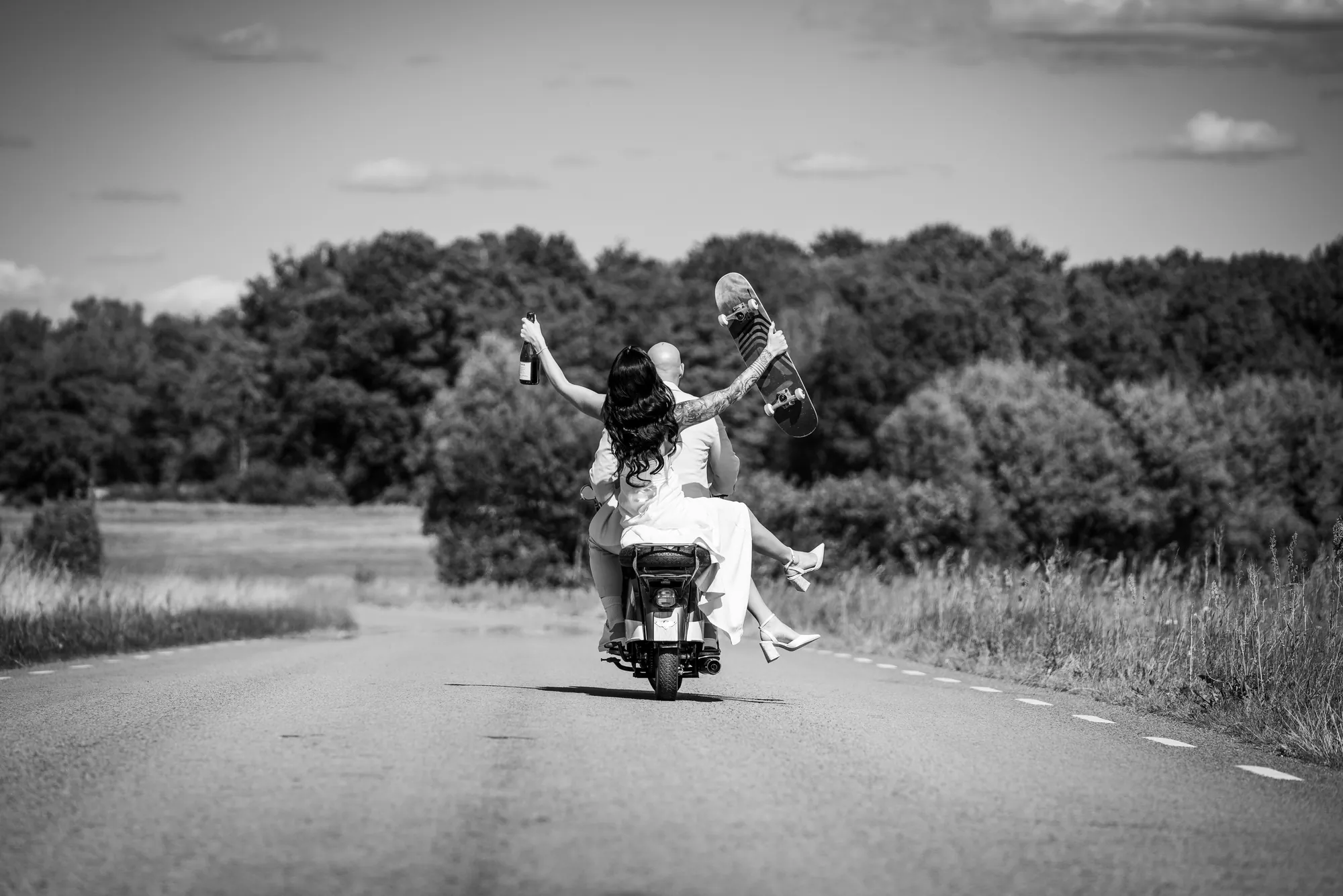 Brudparet kör iväg på moped med champagne och skateboard i händerna, Vinslöv