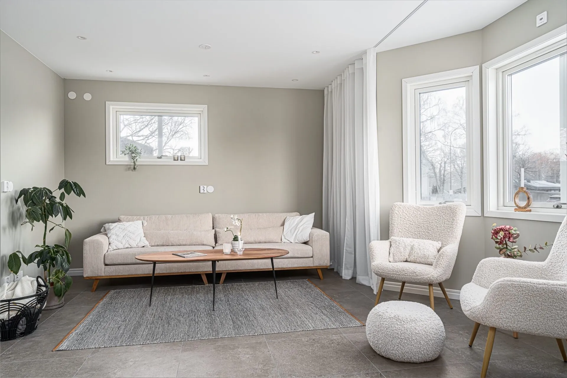Ljust vardagsrum med beige soffa och stora fönster fotograferat åt HusmanHagberg