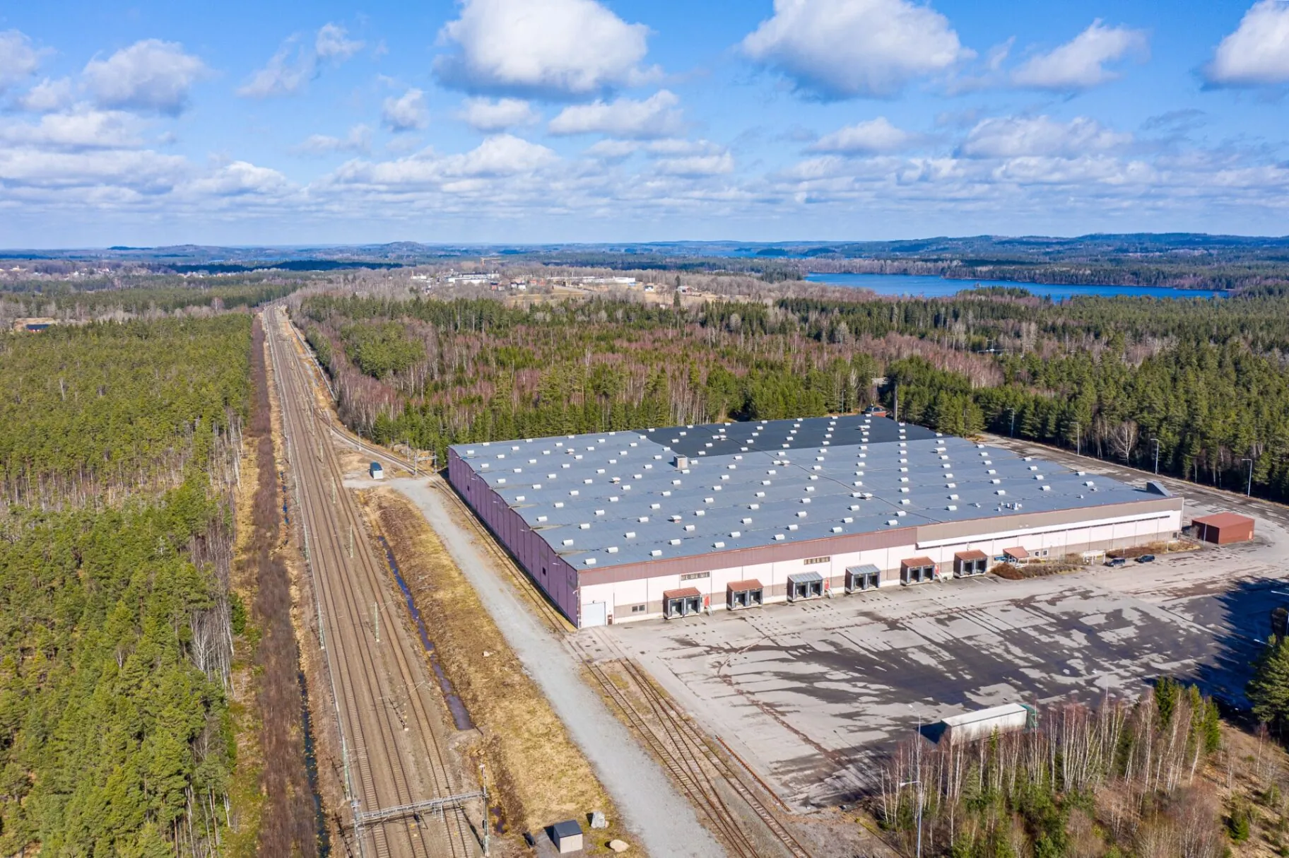 Flygfoto över logistikbyggnad intill järnvägsspår och skog