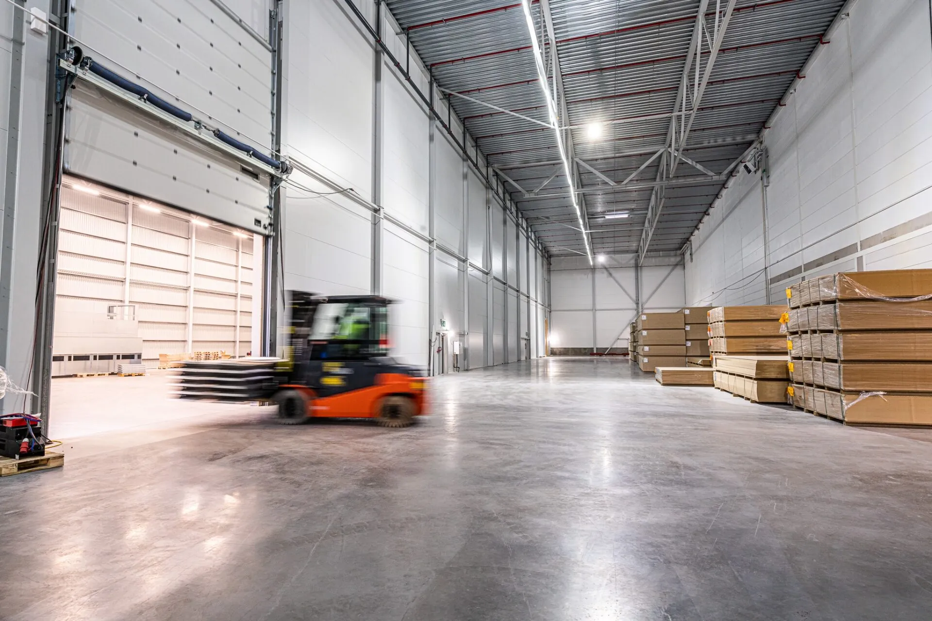 Truck i rörelse genom lagerhall med högt i tak och pallar på golvet